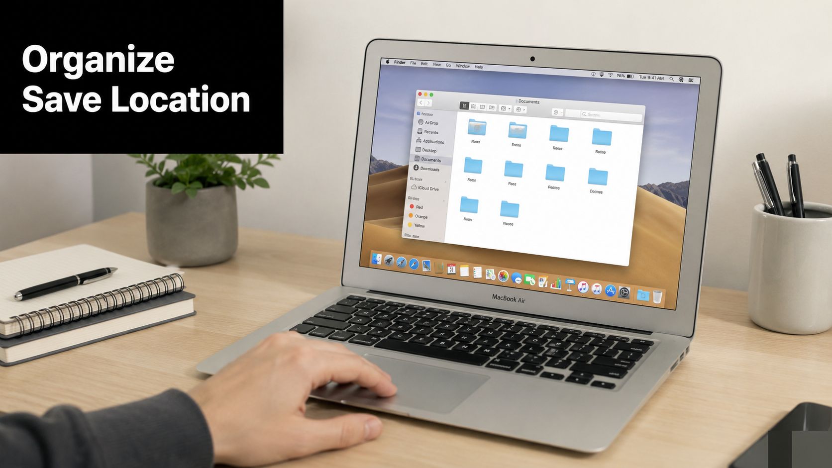 A person using a MacBook Air on a wooden desk to organize files in a folder.